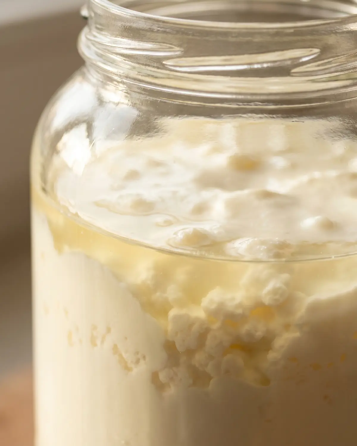 Gros plan vertical d&rsquo;un k&eacute;fir de lait en bocal, avec la s&eacute;paration visible entre s&eacute;rum et cr&egrave;me.