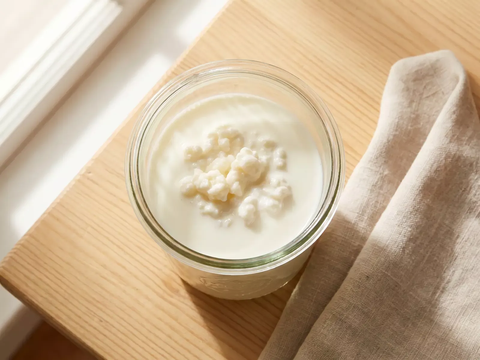 Bocal de k&eacute;fir de lait en fermentation vu de dessus, pos&eacute; avec un linge en lin sur une table en bois.