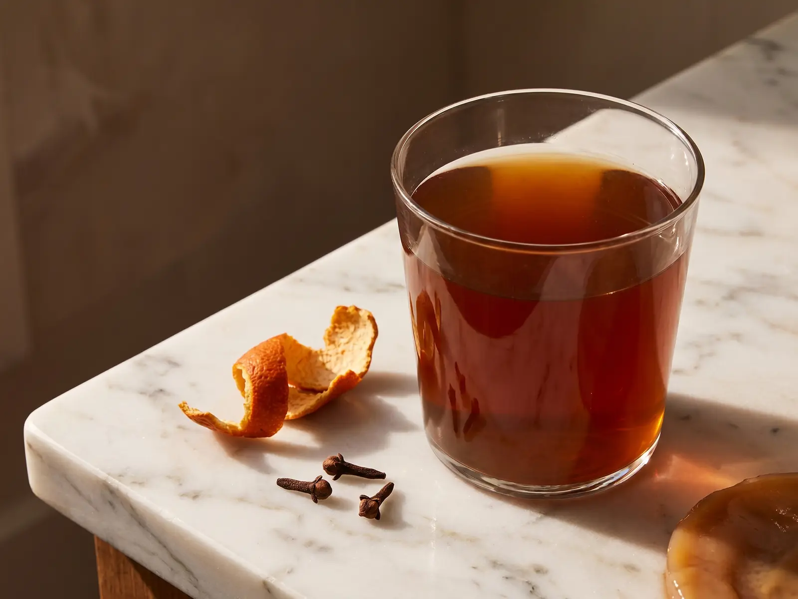 Kombucha ambr&eacute; servi avec clou de girofle et zeste d&rsquo;orange s&eacute;ch&eacute;e sur marbre blanc.
