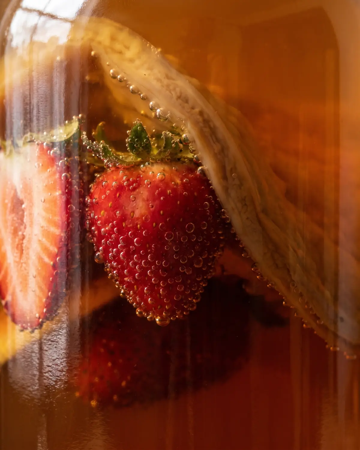Fraise visible dans une bouteille de kombucha, entour&eacute;e de bulles fines contre le verre.
