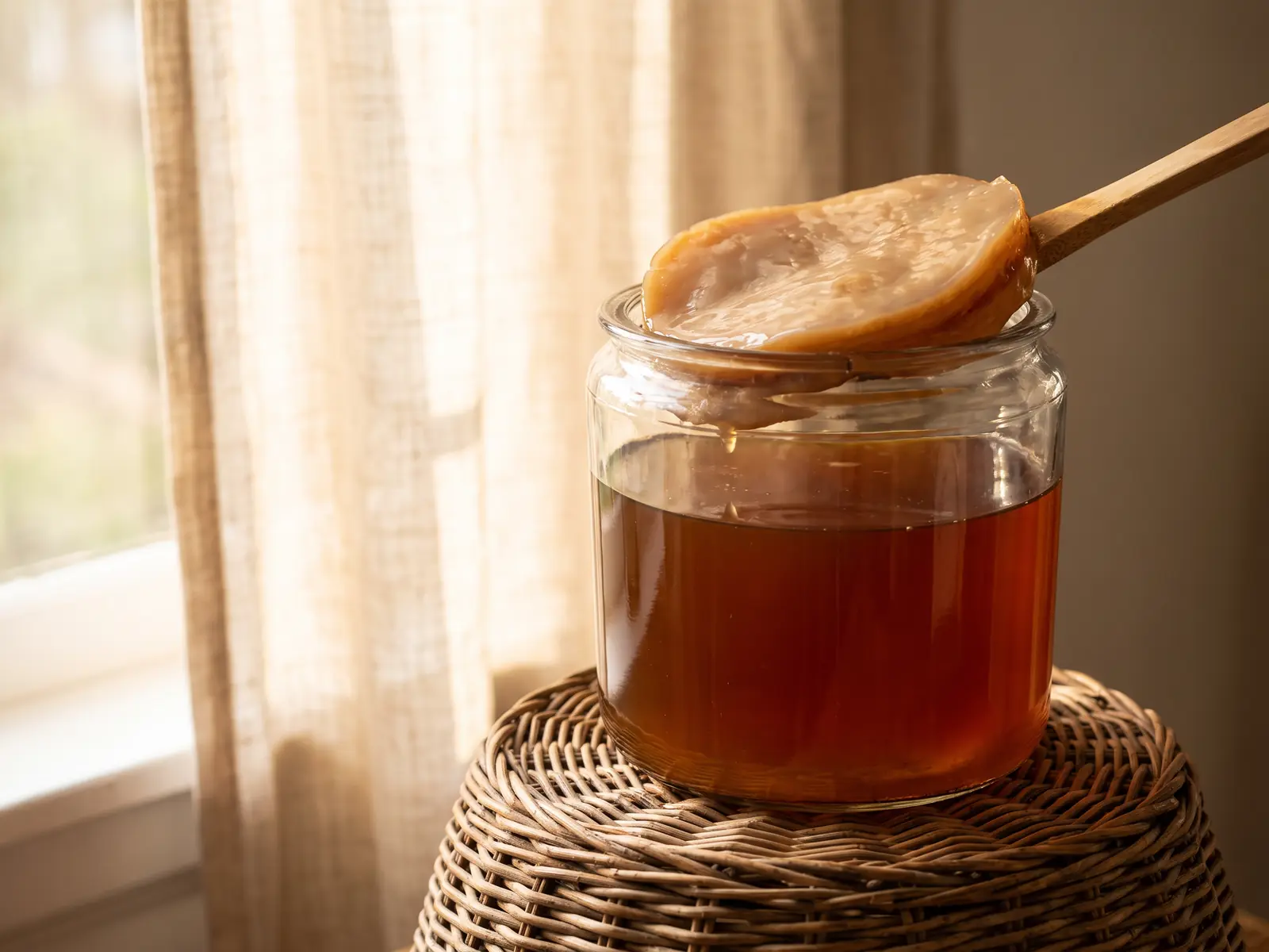 composition kombucha Bocal de SCOBY sur un panier en osier, près de tasses en céramique et d’un rideau de lin lumineux