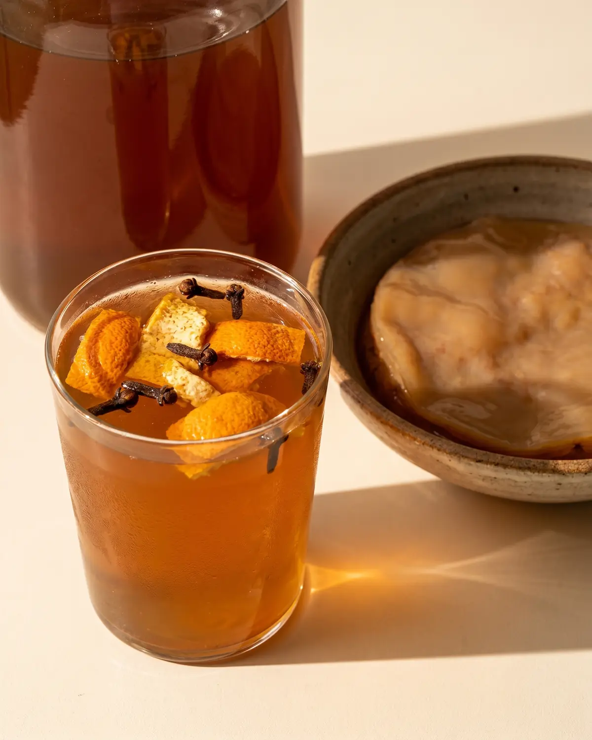 kombucha bienfaits perte de poids Verre de kombucha ambré avec peau d’orange sèche, clou de girofle et lumière douce de fin de journée.